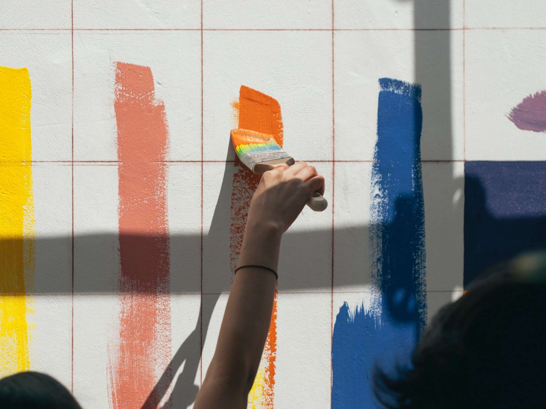Painters using paint rollers to apply multiple lines of paint to a wall