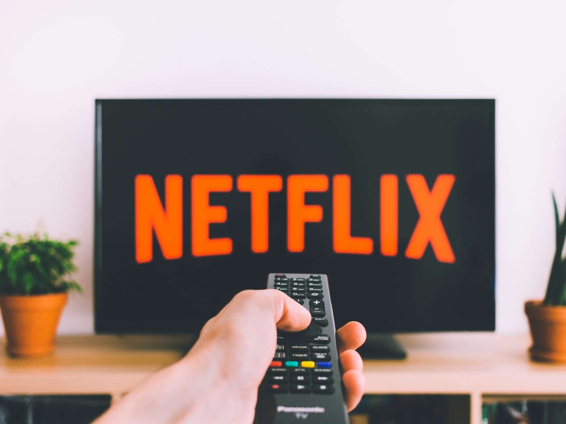 Hand pointing TV remote control at a screen showing Netflix on it