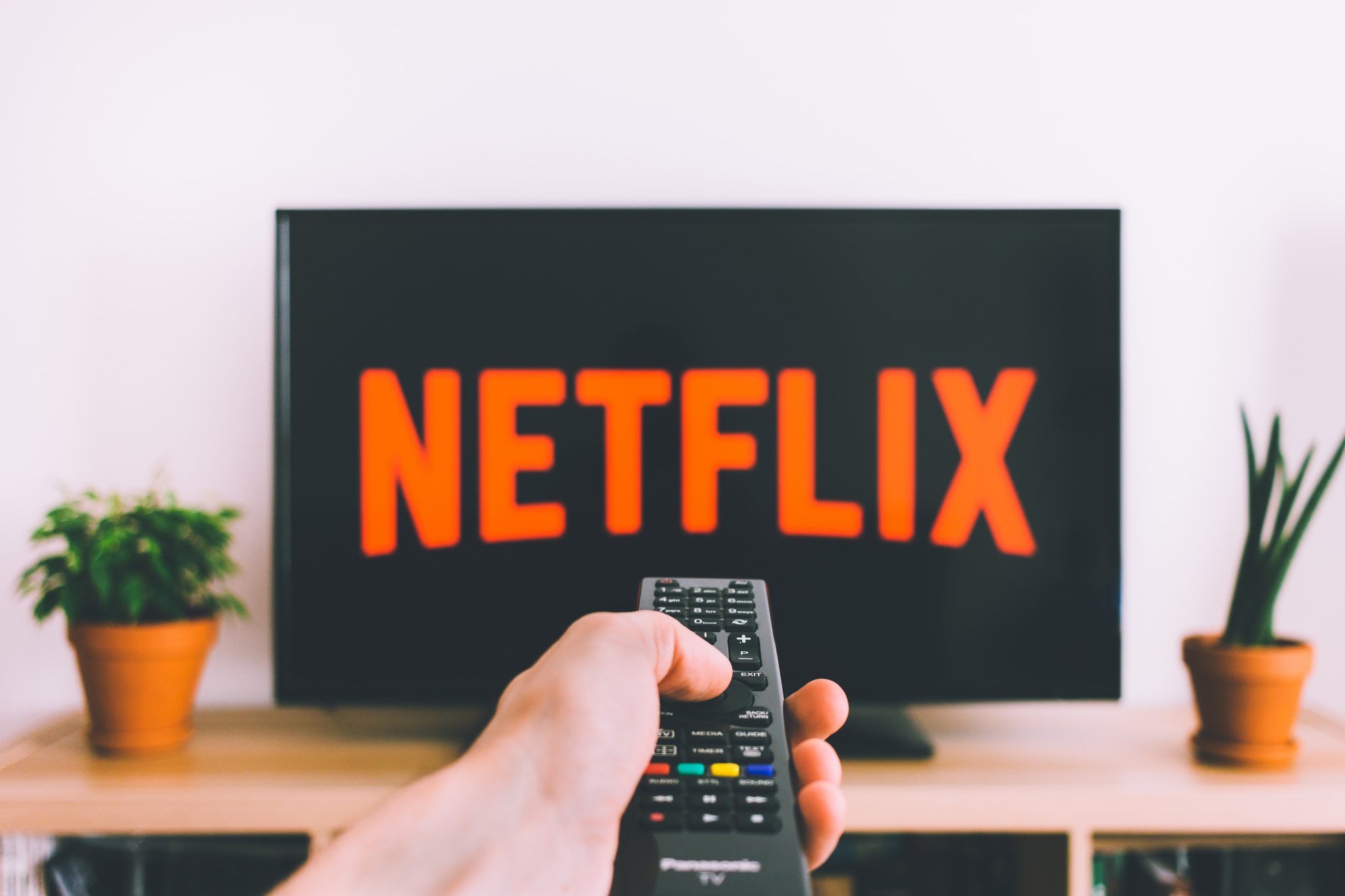 Hand pointing TV remote control at a screen showing Netflix on it