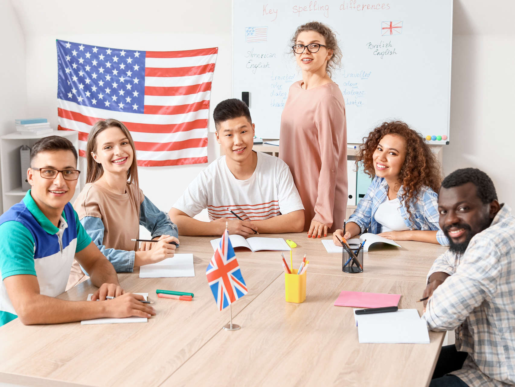 Students of various ethnic backgrounds sit around a table in front of an American flag