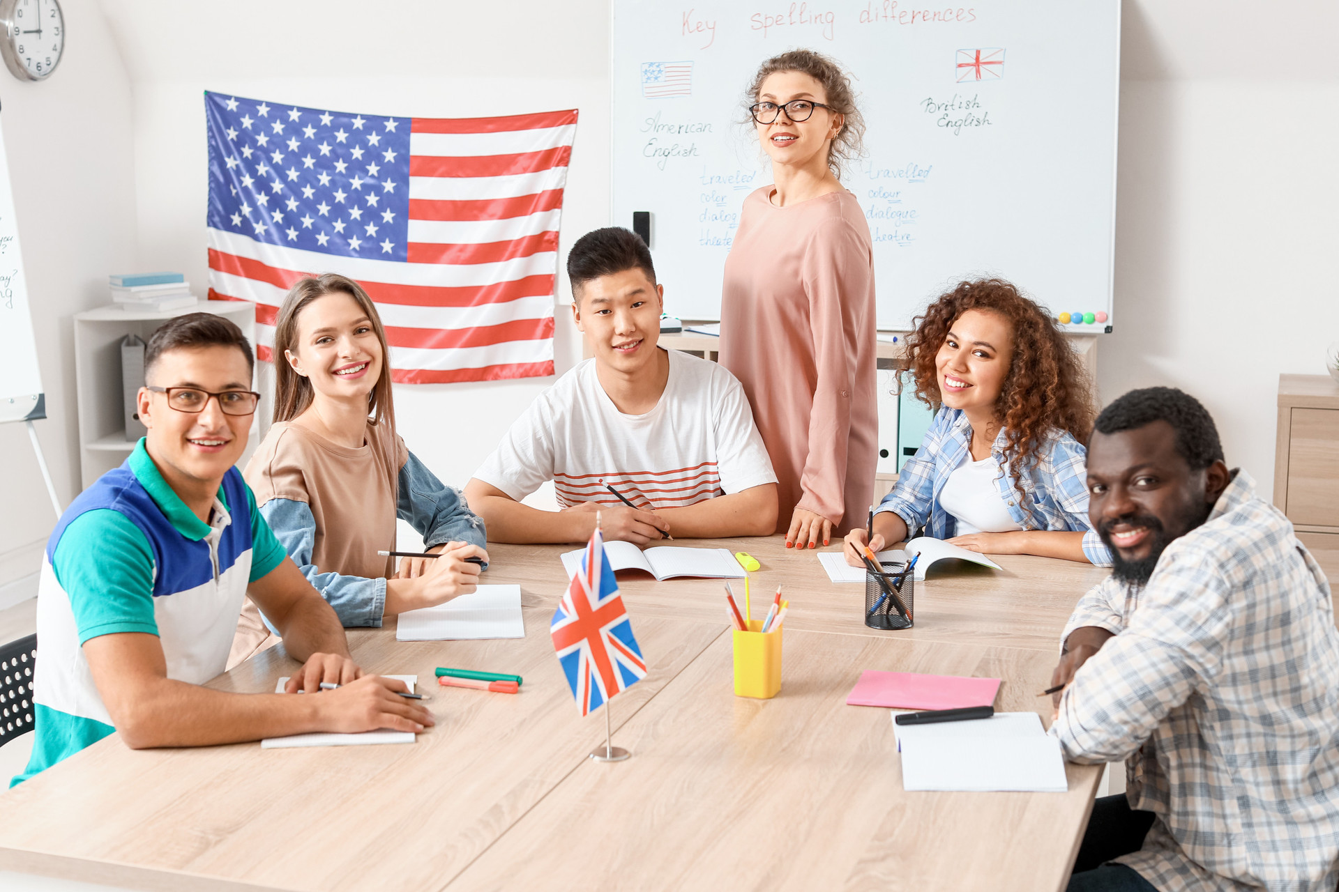 Students of various ethnic backgrounds sit around a table in front of an American flag