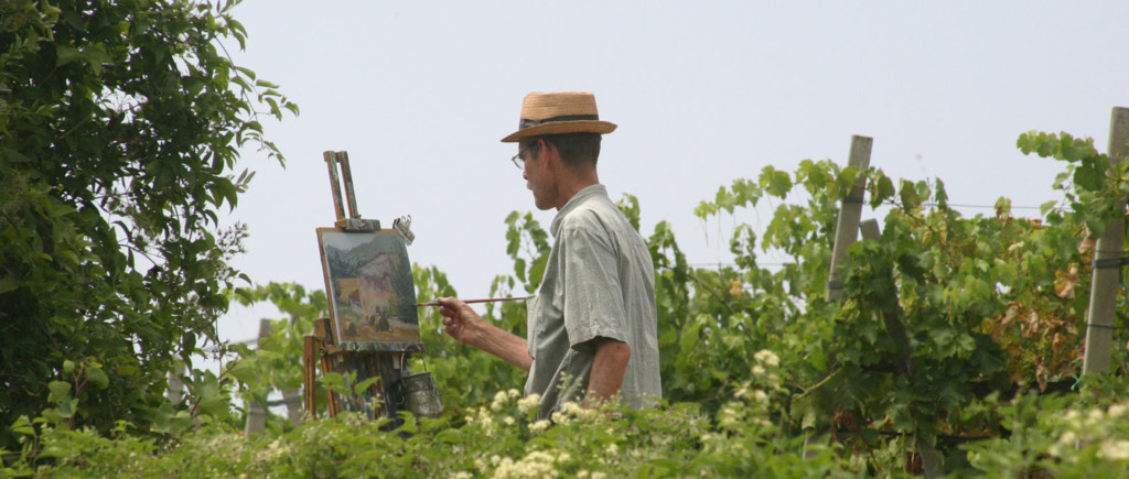 Man in a straw hat standing in a vineyard, painting
