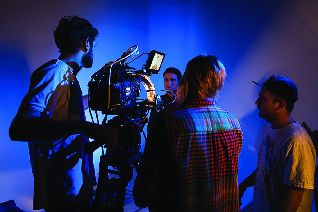 Three students operating a large movie camera, filming a fourth student